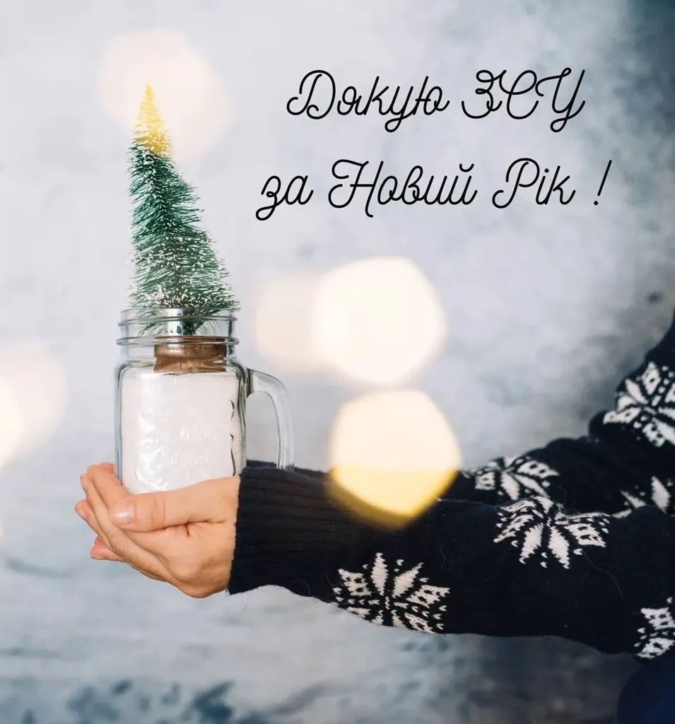 Рука тримає скляну банку з мініатюрною ялинкою та снігом на фоні світла.