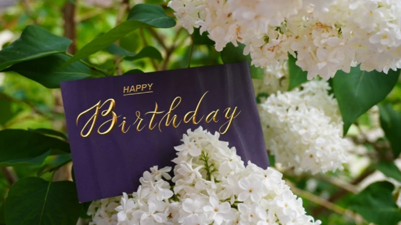 Пурпурна картка з написом Happy Birthday серед білих лілій.