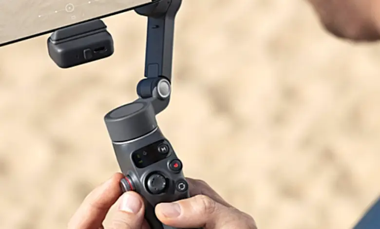Людина тримає стабілізатор для смартфона від DJI на пляжі.