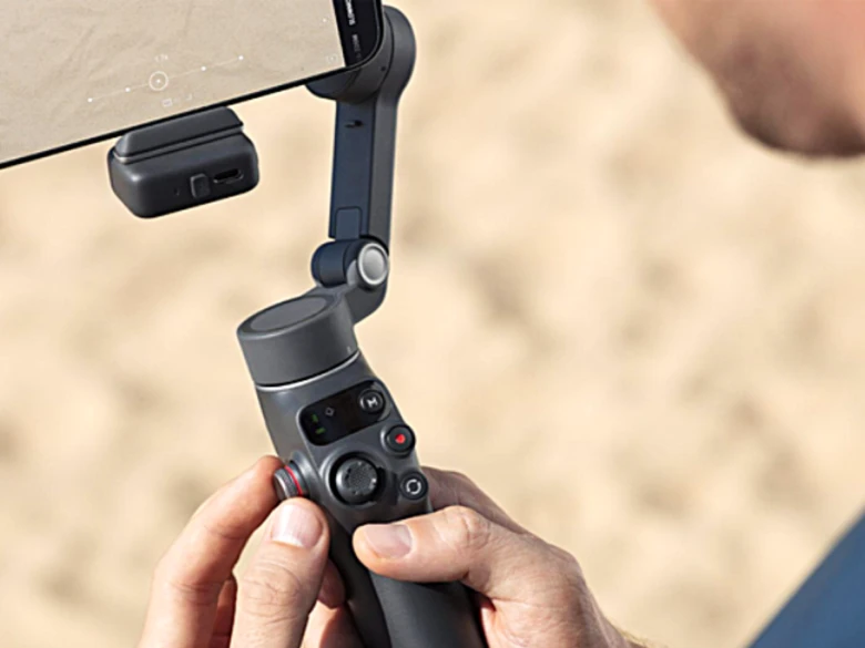 Людина тримає стабілізатор для смартфона від DJI на пляжі.