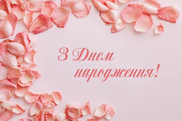 Розові пелюстки троянд на фоні з привітанням з днем народження українською.
